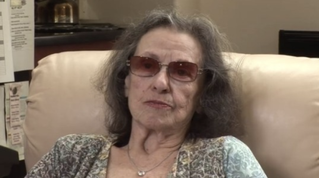 Katherine MacGregor older wearing sunglasses whilst sitting on a sofa
